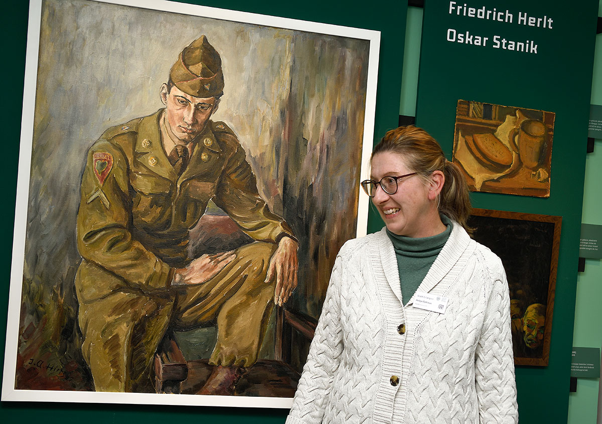 Helga Zahlaus, die gemeinsam mit Andreas Thum die Ausstellung eingerichtet hat, vor einem Gemälde von Joseph Albert Hirtz aus dem Jahre 1947: „Porträt eines GI“