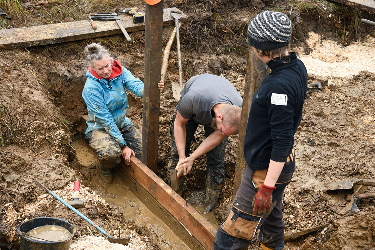 Ein Stauwerk ist am Entstehen: Im morastigen Graben werden Bohlen aufeinander genagelt.